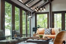 a modern sunroom with skylights and a series of windows, an amber leather sofa and grey and black leather chairs, a bold rug and cool lamps