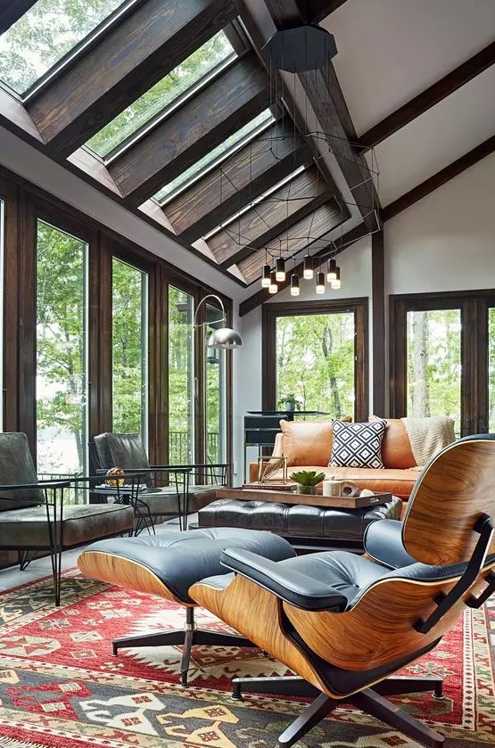 a modern sunroom with skylights and a series of windows, an amber leather sofa and grey and black leather chairs, a bold rug and cool lamps