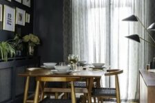 a moody mid-century modern dining space with a stained table and dolg chairs, a black credenza, a stained cabinet with black lamps and a gallery wall