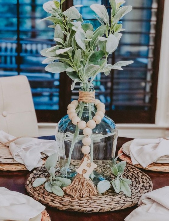 a pretty centerpiece with twine, wooden beads, greenery on a wicker placemat is a chic and cool idea