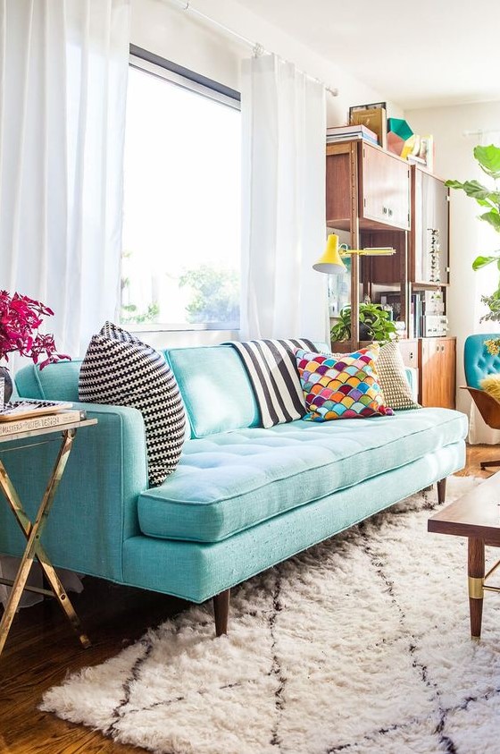 a pretty living room with a modern turquoise sofa, a modern storage unit, a coffee table and touches of gold here and there