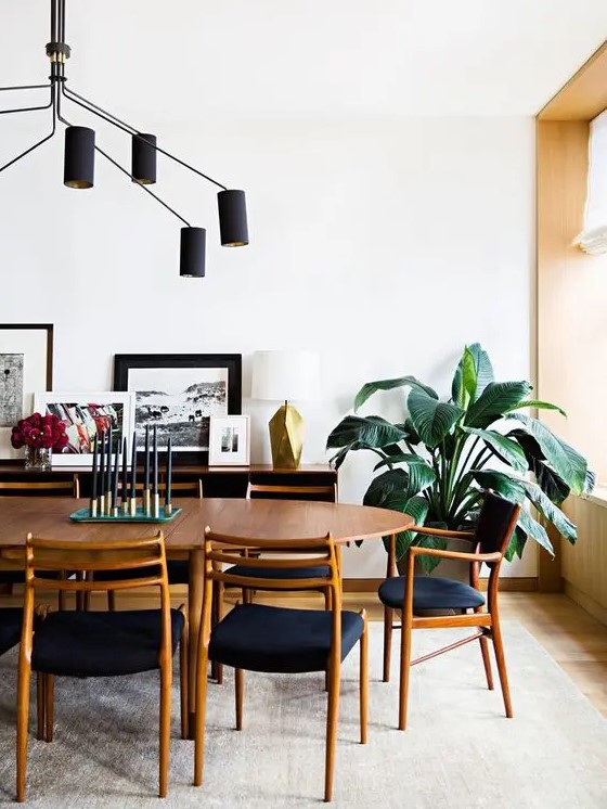 a pretty mid-century modern dining room with a stained dining table, navy chairs, a sideboard with a gallery wall and a black chandelier