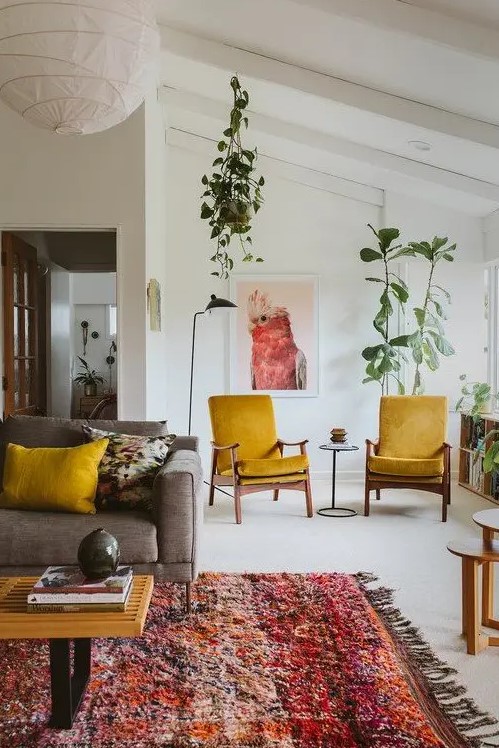 a pretty mid century modern living room with a grey sofa, mustard chairs and pillows, a colorful rug, potted plants and round tables