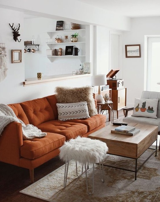 a pretty neutral living room in boho style, with a rust-colored modern sofa, a low table and a fur stool, printed textiles is very welcoming