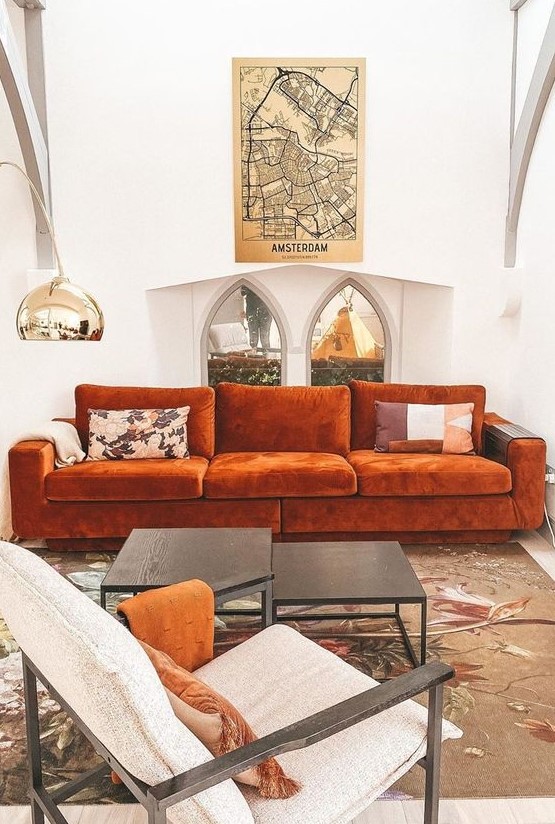 a refined living room with a rust-colored mid-century modern sofa, a duo of tables, a creamy chair, a polished floor lamp is amazing