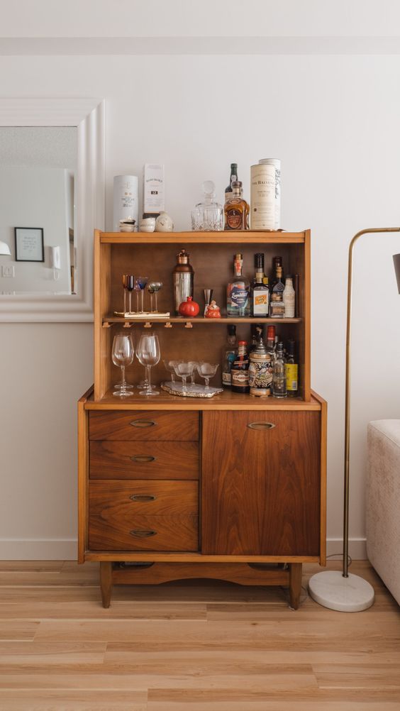 a rich-stained mid-century modern cabinet with shelves and drawers is a home bar for a modern space