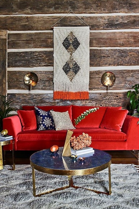 a rustic living room with wood wallpaper walls, a bold red sofa, a refined blue marble table and touches of gold here and there