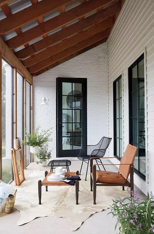 a small and elegant modern sunroom with a coffee table, a black metal and an amber leather chair, potted plants and a rug