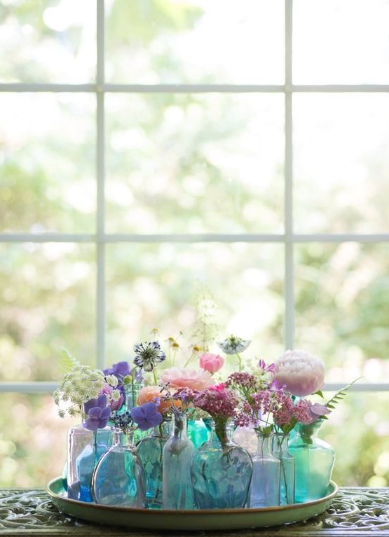 a tray with an arrangement of blue and green bottles and vases with colorful blooms