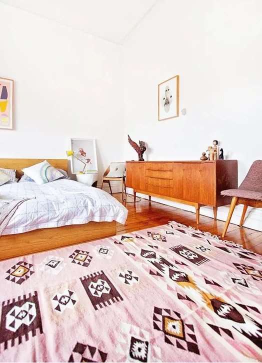 a welcoming and bright mid-century modern space with warm-stained wooden furniture, a pink rug and some artworks