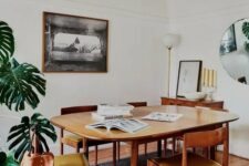 a welcoming mid-century modern dining space with a stained table, mustard chairs, a sideboard, a potted palm tree and a mirror