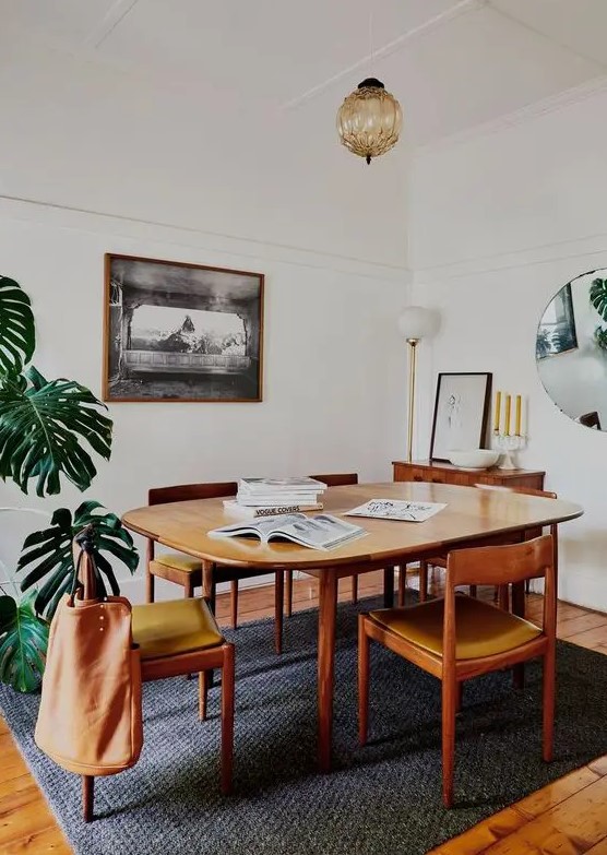 a welcoming mid-century modern dining space with a stained table, mustard chairs, a sideboard, a potted palm tree and a mirror