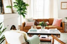 a welcoming mid-century modern lviing room with a non-working fireplace, an amber leather sofa, white chairs, a low coffee table, a mirror and pastel pillows