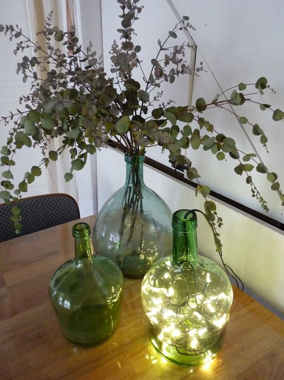 an arrangement of green bottles with lights, with dried eucalyptus is a cool decoration idea for your space