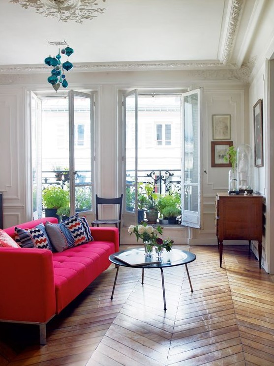 an elegant living room with a hot pink tufted sofa, a low table, a wooden sideboard and lots of potted plants in the balcony