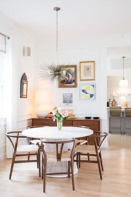 an elegant mid-century modern dining nook with a stained credenza, a round table and stained chairs, a gallery wall and a sunburst chandelier