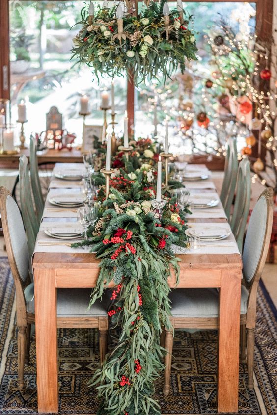 an evergreen and greenery garland with pinecones, cranberries and white blooms plus tall and thin candles for Christmas