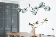 an exquisite mid-century modern dining room with a stained table, black chairs, a green rug, a green chandelier and a storage unit