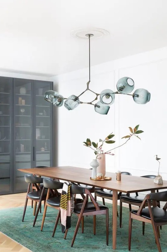 an exquisite mid-century modern dining room with a stained table, black chairs, a green rug, a green chandelier and a storage unit