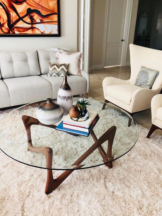 an eye-catchy mid-century modern coffee table with a round clear glass tabletop and a quirky dark stained wooden base is wow