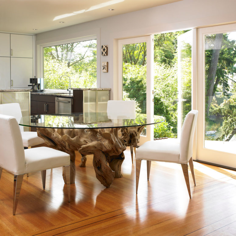 a large round dining table with a glass tabletop and a driftwood base for a slight sea-inspired space (The Sky is the Limit Design)