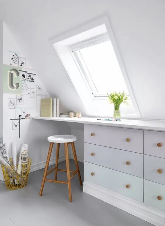 a Nordic attic home office in white, with a skylight, a built-in desk, a stool and a small gallery wall plus blooms