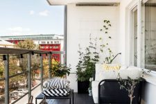 a Nordic balcony with a black floor, black furniture with printed and neutral upholstery, potted blooms and candle lanterns