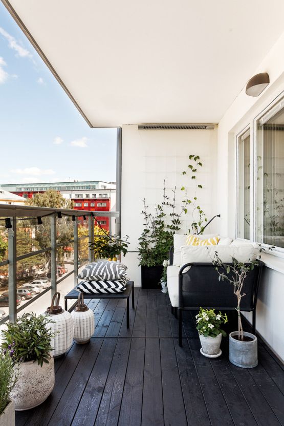 a Nordic balcony with a black floor, black furniture with printed and neutral upholstery, potted blooms and candle lanterns