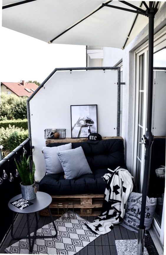 a Nordic balcony with a pallet loveseat with black upholstery, printed rugs and blankets, a black side table and a succulent