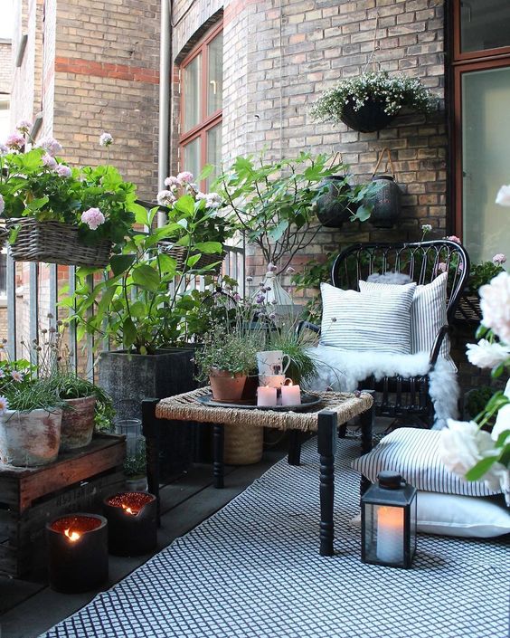 a Nordic balcony with a printed rug, a black chairs and a woven table, potted greenery, candle lanterns and candle holders is amazing