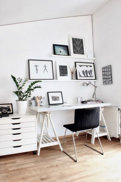 a Nordic home office with a white trestle desk, a black chair, a file cabinet, a ledge gallery wall and a table lamp, potted greenery