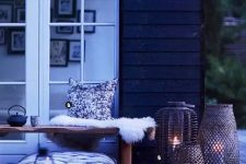 a Nordic summer terrace in black and white, with a bench, faux fur, pillows, wicker and glass candle holders