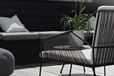 a Nordic terrace with a grey deck, a black built-in bench, a black chair with white upholstery and greenery