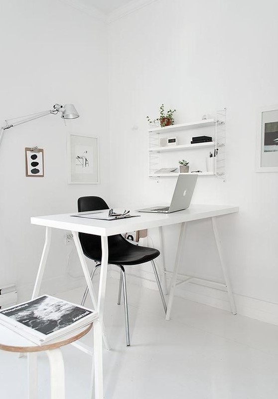 a Nordic white workspace with a white desk, a shelving unit, artworks and a little stool by the desk