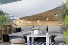 a Scandi terrace with a grey sectional, a coffee table, string lights, potted greenery and jute poufs