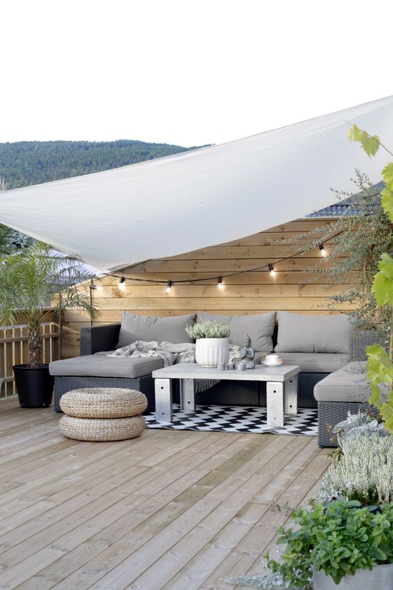 a Scandi terrace with a grey sectional, a coffee table, string lights, potted greenery and jute poufs a Scandi terrace with a grey sectional, a coffee table, string lights, potted greenery and jute poufs