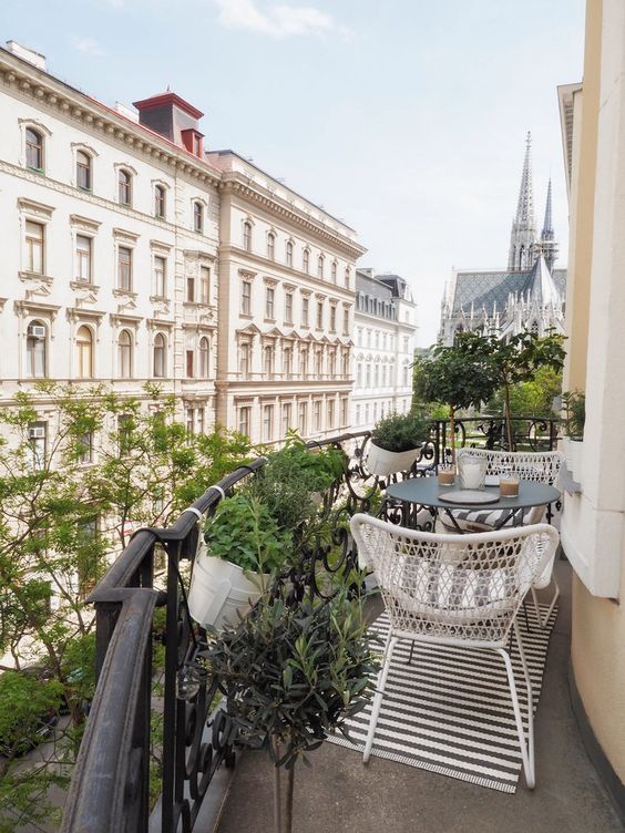 a Scandinavian balcony with a striped rug, white chairs and a black coffee table, potted greenery and fantastic views of Vienna