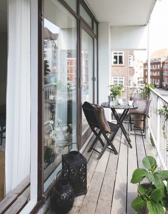 a Scandinavian balcony with black folding chairs and a table, black candle lanterns, potted greenery and blooms