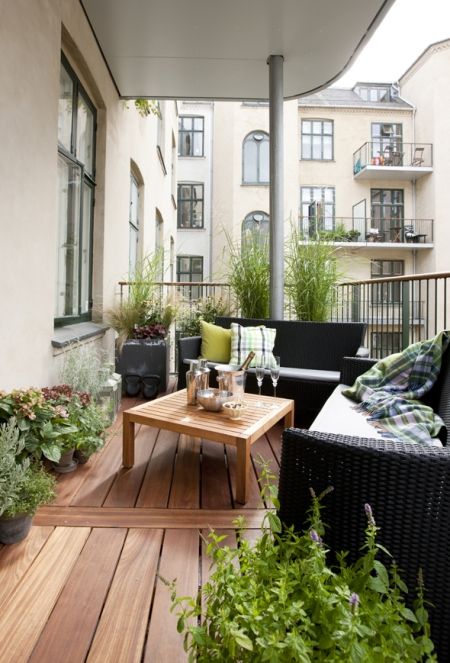 a Scandinavian balcony with black wicker furniture, a stained table, potted plants and blooms and printed textiles