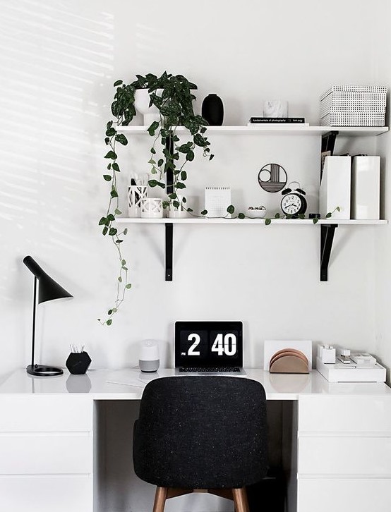 a Scandinavian home office nook with a white desk, a black chair, lamp and some wall-mounted shelves