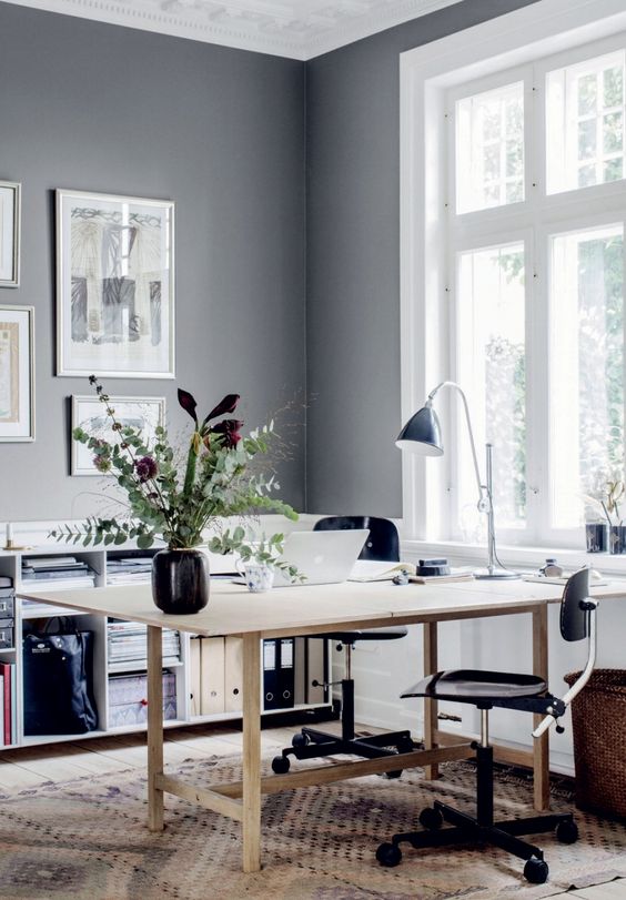 a Scandinavian home office with a wooden desk, black chairs, a gallery wall, a black lamp, a storage unit and a rug