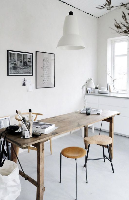 a Scandinavian home office with a wooden desk, cork stools and a wooden chair, a pendant lamp, artworks and a built-in storage unit