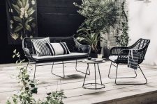 a Scandinavian outdoor space with elegant metal and wicker furniture, wooden decks and potted greenery and a tree