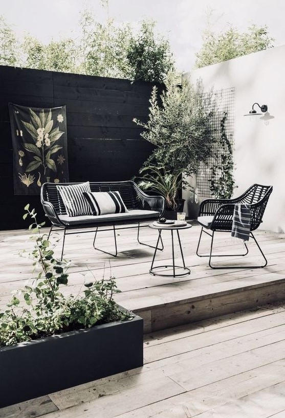 a Scandinavian outdoor space with elegant metal and wicker furniture, wooden decks and potted greenery and a tree