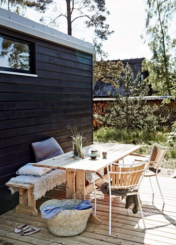 a Scandinavian terrace with a dining zone with wooden furniture and forged chairs, a basket and some greenery