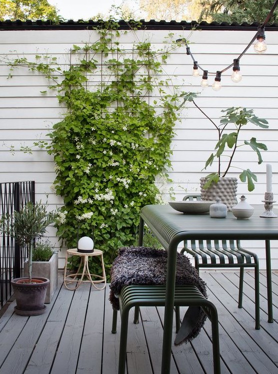 a Scandinavian terrace with dark green metal furniture, climbing greenery and blooms, potted plants and a rattan chair a Scandinavian terrace with dark green metal furniture, climbing greenery and blooms, potted plants and a rattan chair