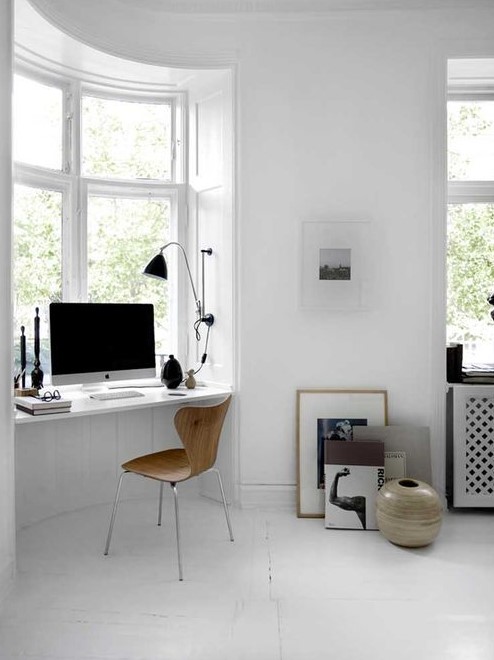 a Scandinavian white workspace with a windowsill desk, a wooden chair, some dramatic touches of black and art