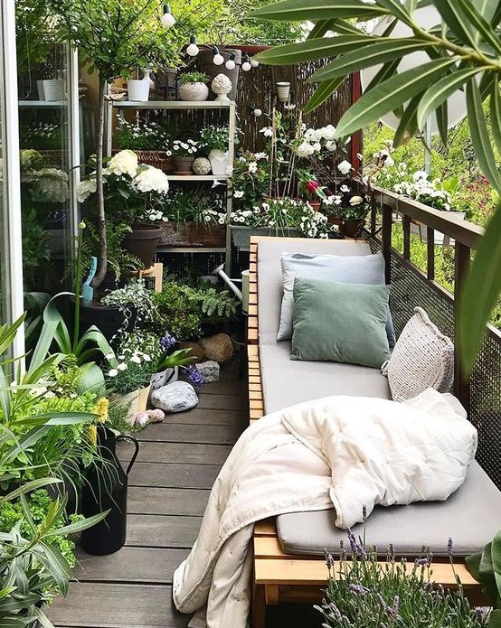a balcony garden with potted greenery and blooms and a wooden lounger with upholstery and pillows is a gorgeous place to be