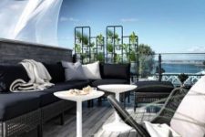 a beautiful contemporary seaside terrace with dark wicker furniture and black upholstery, white coffee tables and a chair, black and white pillows