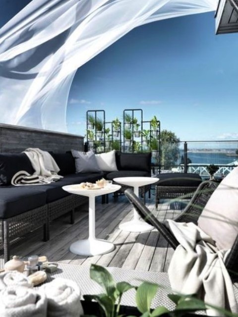 a beautiful contemporary seaside terrace with dark wicker furniture and black upholstery, white coffee tables and a chair, black and white pillows